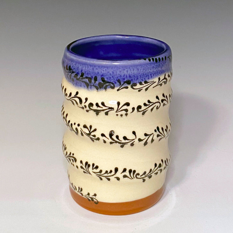 Red earthenware clay vase with white background. Decorated with black scrollwork, glazed blue on the inside and over the rim.