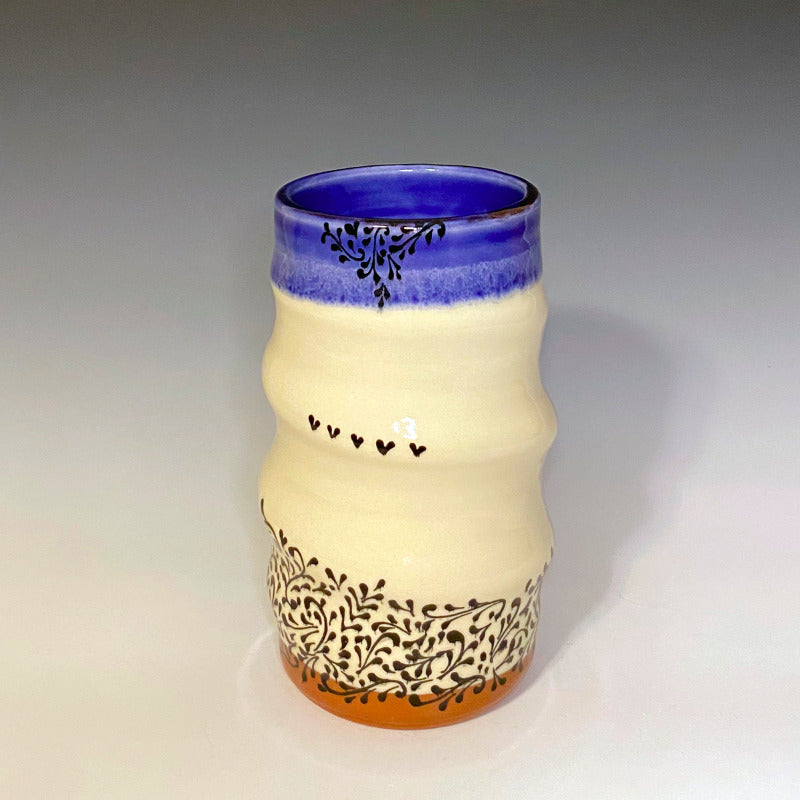 Red earthenware clay vase with white background. Decorated with black scrollwork, glazed blue on the inside and over the rim.
