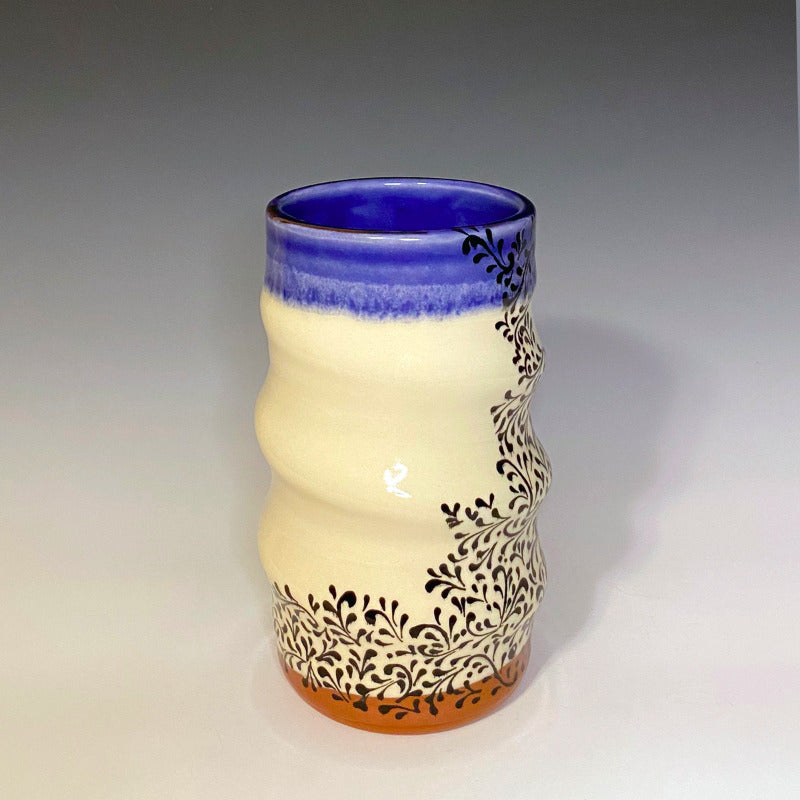Red earthenware clay vase with white background. Decorated with black scrollwork, glazed blue on the inside and over the rim.