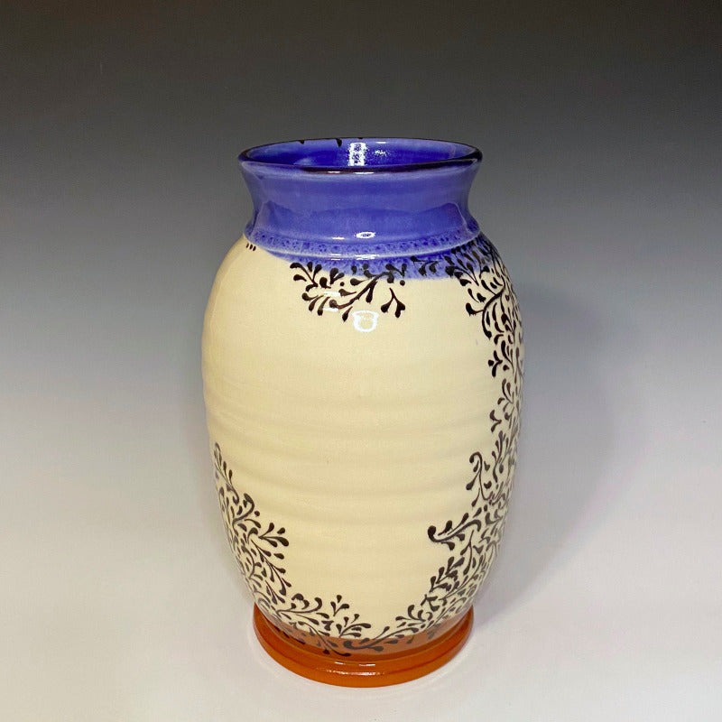 Red earthenware clay vase with white background. Decorated with black scrollwork, glazed blue on the inside and over the rim. 