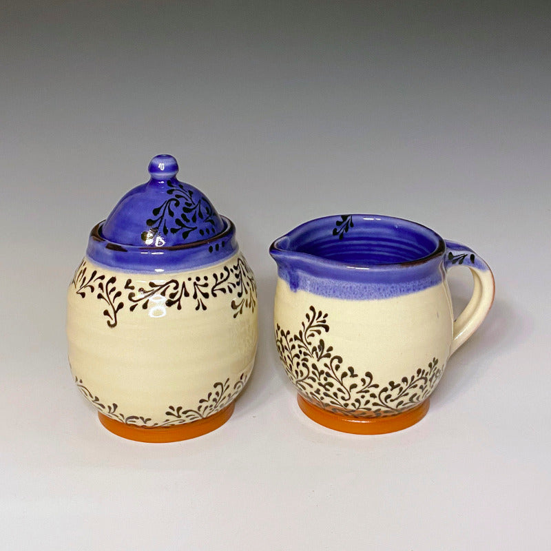 Lidded sugar jar and handled creamer set. Red earthenware with white background, blue inside, and black scroll decoration.